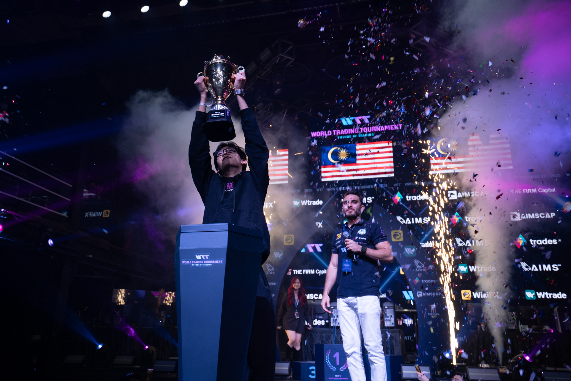 A World Trading Tournament champion lifting the trophy on stage amid smoke and confetti